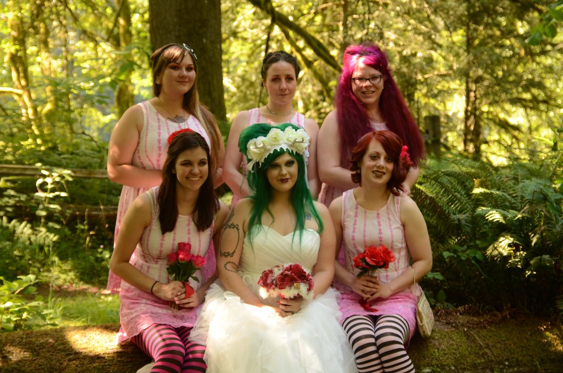 Bride seated with five bridesmaids in pink tie-dye dresses among the ferns at Oxbow Park