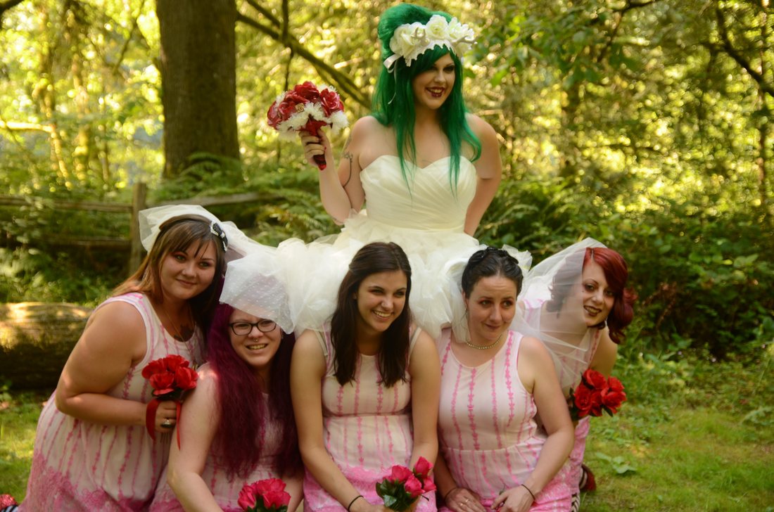 Bride standing behind her five bridesmaids, all holding red carnations, in the forest