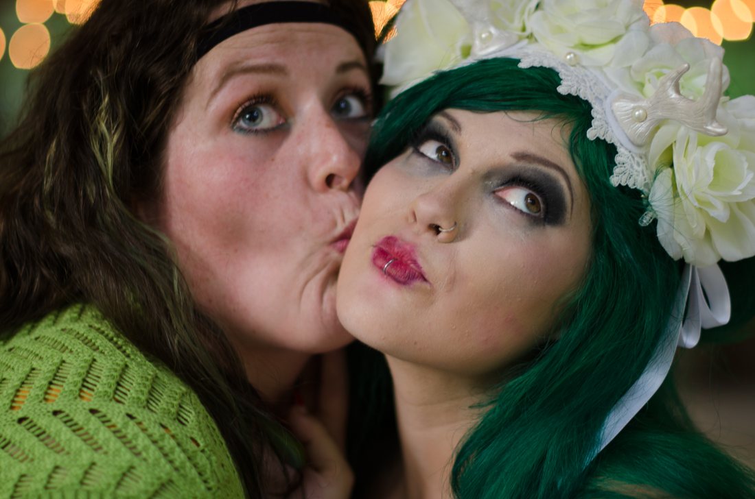 Guest kissing the bride on the cheek, both pulling faces, warm bokeh behind