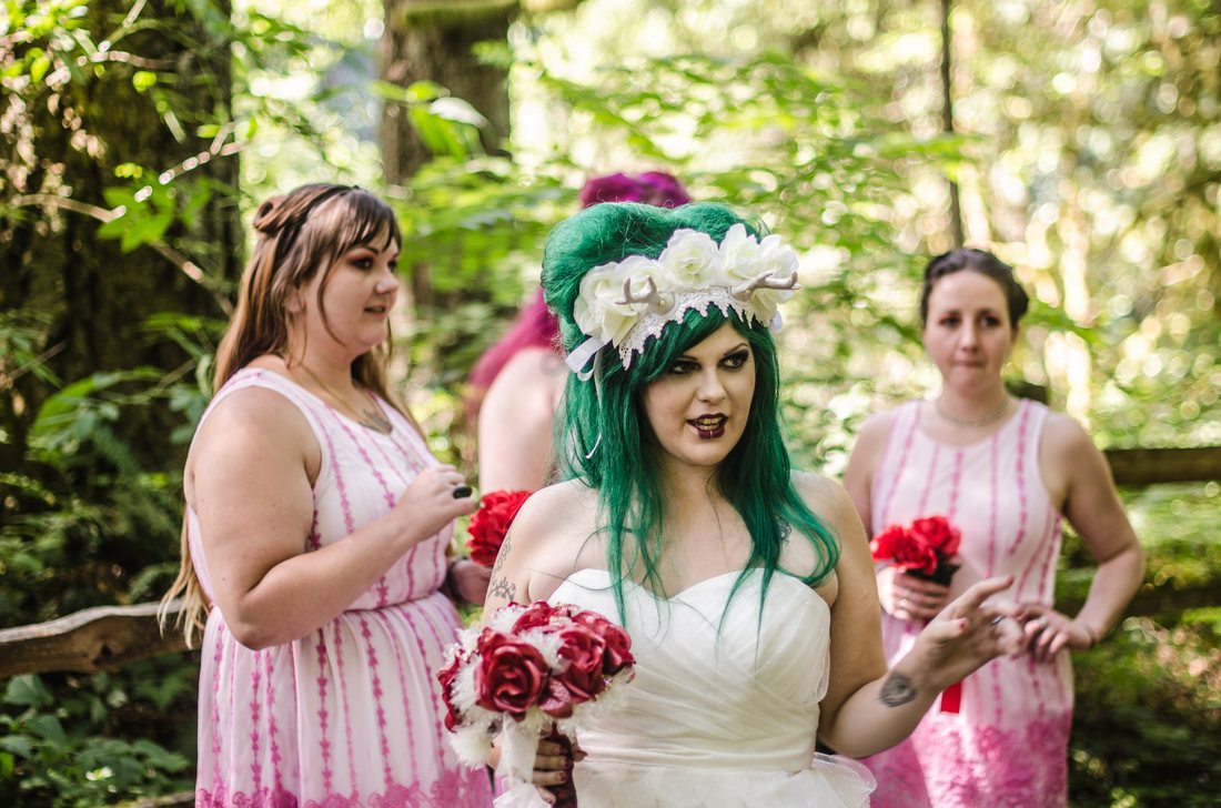 Bride holding her red and white bouquet, bridesmaids behind her in the trees