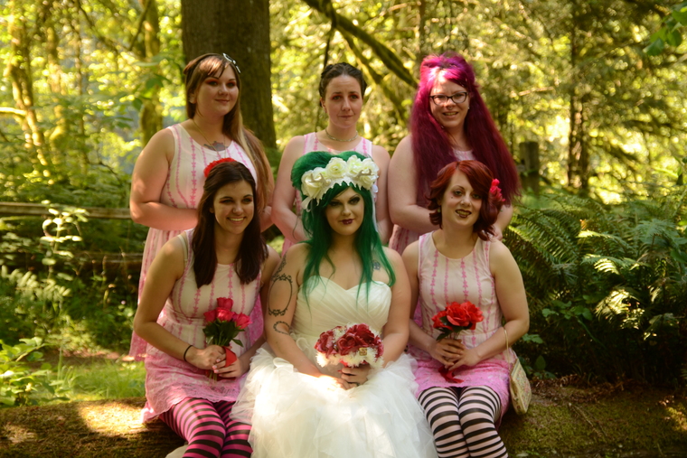 Bride with green hair and groom embrace near wedding signs in woods